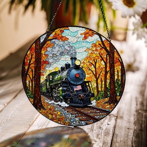 May include: Circular stained glass window depicting a vintage train in an autumnal forest. The train is black and green with a red accent and an American flag. The window is framed with a black metal chain, with the scene in shades of orange and brown.