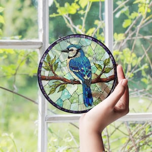 a hand holding a stained glass bird on a tree branch