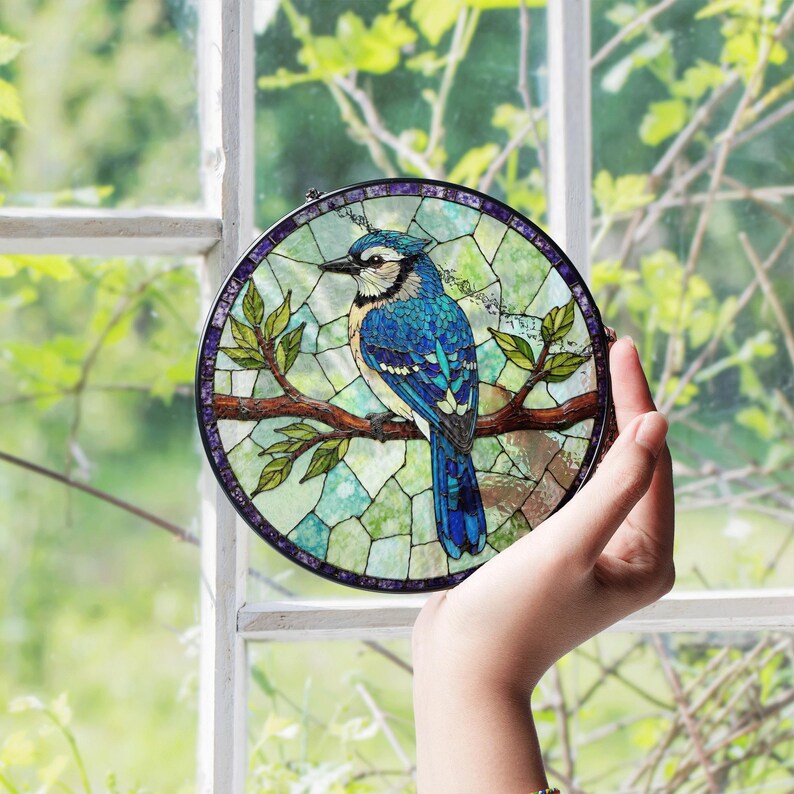 a hand holding a stained glass bird on a tree branch
