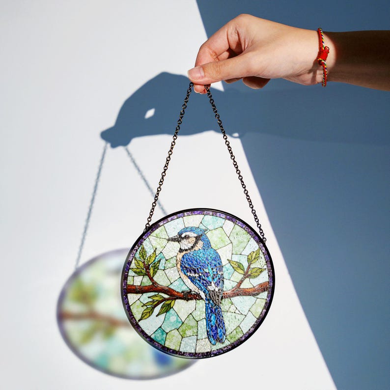 a hand holding a stained glass bird hanging from a chain