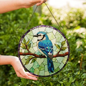 a hand holding a stained glass bird on a branch