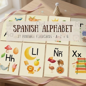 Può includere: Un set di 27 flashcard stampabili dell'alfabeto spagnolo, dalla A alla Z e Ñ. Ogni carta mostra una lettera in carattere nero accanto a colorate illustrazioni ad acquerello di oggetti, animali e cibo. Il testo recita SPANISH ALPHABET 27 PRINTABLE FLASHCARDS A-Z + Ñ.