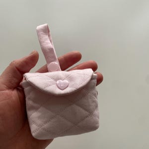 May include: A pink quilted fabric pouch with a heart-shaped button and a fabric loop handle.