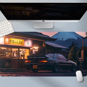 May include: A black sports car is parked in front of a Japanese restaurant with a mountain in the background. The scene is depicted on a large rectangular mousepad. A computer monitor, keyboard, and mouse are visible.