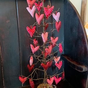 May include: A twig tree decorated with red and white fabric hearts. The tree is in a brown pot with green moss.