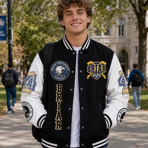 May include: Black and white varsity jacket with the text "Briar University" and patches. The jacket has white sleeves, a black body, and a white and black striped collar and cuffs. Patches include a hockey logo and the number "4".