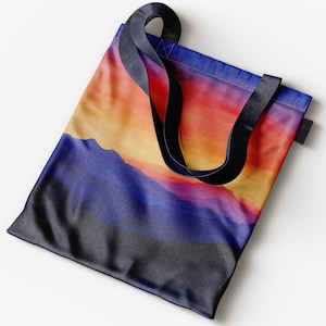 K&ouml;nnte beinhalten: Eine Tragetasche mit schwarzen Henkeln und einem farbenfrohen Sonnenuntergangs-Landschaftsdruck. Die Tasche zeigt einen Farbverlauf von Orange, Gelb, Rosa und Lila mit einem dunkelblauen Gebirgszug im Vordergrund.