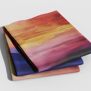 K&ouml;nnte beinhalten: Drei gefaltete Stoffquadrate mit einem Aquarell-Sonnenuntergangsdesign. Das obere Quadrat ist leuchtend orange, gelb und rosa, das mittlere Quadrat ist dunkelblau und das untere Quadrat ist hellpfirsich.