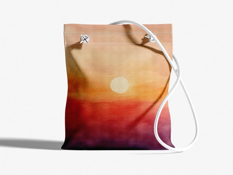 K&ouml;nnte beinhalten: Eine wei&szlig;e Canvas-Tragetasche mit einem auf die Vorderseite gemalten Sonnenuntergang. Der Sonnenuntergang ist ein Farbverlauf von Orange, Rot und Lila mit einem wei&szlig;en Kreis in der Mitte.