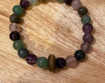 May include: A multi-colored beaded bracelet with green, purple, and brown beads. The bracelet has a wooden bead in the center.