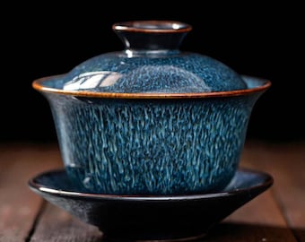 May include: A blue ceramic gaiwan tea set with a matching lid and saucer. The gaiwan has a textured surface with a dark brown rim. The set is designed for traditional tea ceremonies.