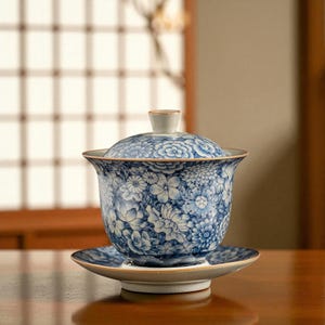 May include: A blue and white floral patterned tea set, including a lidded cup and saucer. The cup and lid feature a delicate floral design in shades of blue and white. The set is likely ceramic and has a gold trim.