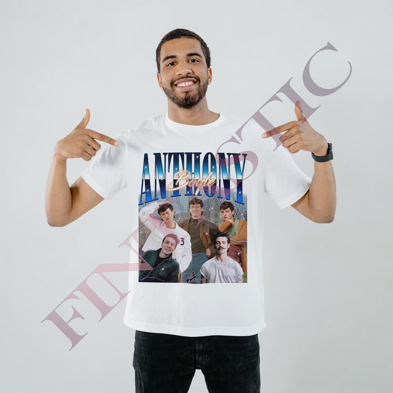 May include: White t-shirt featuring a vintage-style graphic of a group of people with the text "ANTHONY Boyle" in a blue and gold design. The shirt is being pointed at by a person.
