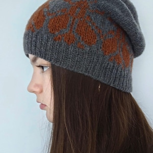 May include: A gray knitted beanie with a brown floral pattern. The beanie is slouchy and has a fold-over brim.