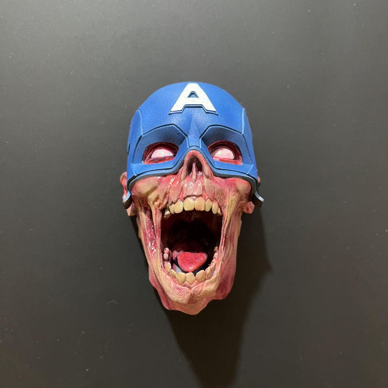 May include: A red and white zombie skull wearing a blue and white Captain America helmet. The skull is open-mouthed with a red tongue sticking out.