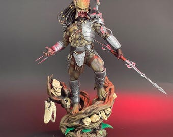 May include: A detailed Predator figure, posed on a tree trunk base decorated with skulls and foliage. The figure wears metallic armour and holds a spear. The Predator's dreadlocks and mandibles are visible, showcasing intricate detailing.