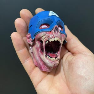 May include: A detailed, hand-painted figurine of a zombie Captain America. The figurine is painted in shades of red, white, and blue, with a realistic depiction of a decaying skull and open mouth. The figurine is wearing a blue and white Captain America helmet.
