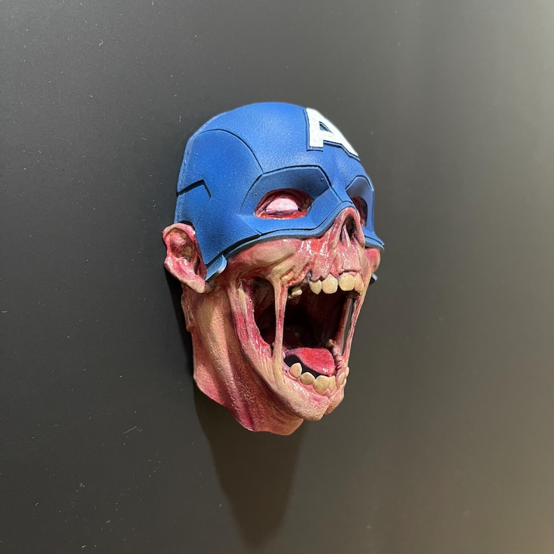 May include: A 3D printed sculpture of a zombie Captain America head with a blue and red helmet and a wide open mouth.