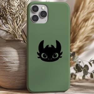 May include: A green phone case featuring a black cartoon dragon design. The case has a smooth finish and a camera cutout. The design is centered on the back of the phone case.