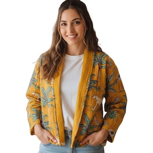 Pode incluir: Casaco mostarda com frente aberta com estampa tropical com palmeiras e chitas. O casaco tem uma textura acolchoada e é usado sobre uma camiseta branca e jeans azuis. Uma opção de roupa exterior elegante e leve.