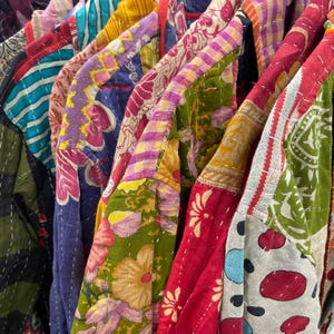May include: A rail of vibrant patchwork jackets. The jackets display diverse patterns, including floral and geometric designs, in shades of red, green, purple, and yellow. Each jacket is unique, with visible stitching.