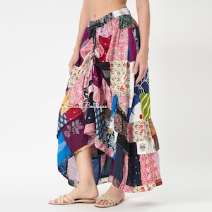 Op de afbeelding: Een lange, zwierige rok met een patchworkontwerp met diverse kleurrijke patronen, waaronder bloemen-, geometrische en paisleyprints in tinten roze, blauw, paars en groen. De rok heeft een taille met trekkoord en een asymmetrische zoom.