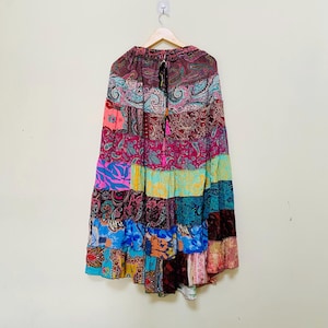 Puede incluir: Una falda patchwork con una variedad de coloridos estampados de cachemira y florales. La falda est&aacute; hecha de m&uacute;ltiples paneles de tela en tonos de rosa, azul, verde y burdeos. Cuelga de una percha de madera.