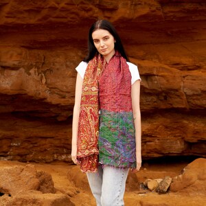 May include: A colorful scarf with a paisley pattern and a patchwork design. The scarf features shades of red, green, and purple. The scarf is draped over a person's shoulders.