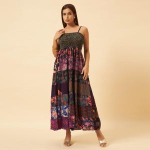 May include: A floor-length maxi dress featuring a smocked bodice and thin spaghetti straps. The dress is constructed from a patchwork of various floral and botanical print fabrics in shades of purple, blue, red, and green, creating a tiered effect.