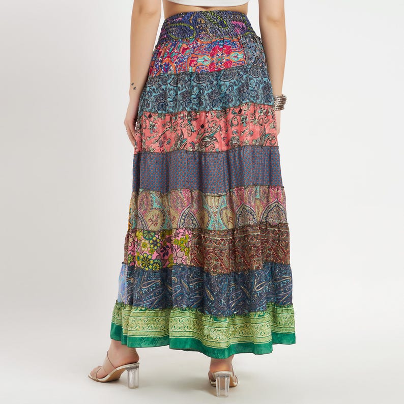 May include: A long, patchwork skirt with a tiered design. The skirt features a variety of colorful paisley and floral patterns in shades of blue, pink, green, and brown. The skirt is made of a lightweight fabric and has an elastic waistband.