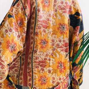 May include: A floral patterned kimono in shades of yellow, orange, and cream. The kimono features large flower designs and a contrasting navy blue trim. The belt is patterned with stripes and floral accents. The garment is made of a soft, quilted fabric.