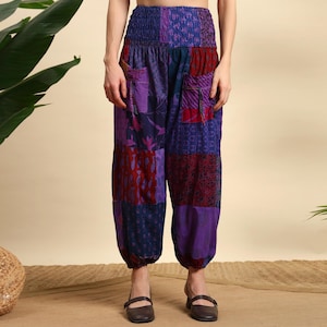 Puede incluir: Pantalones patchwork en tonos morados, rojos y azules. Los pantalones tienen una cintura fruncida y bolsillos. La tela es una mezcla de piezas estampadas y lisas, creando un diseño único. Los pantalones tienen un ajuste relajado y cómodo.