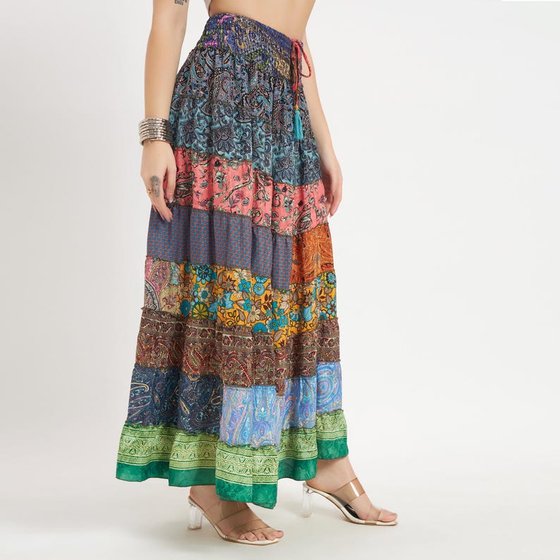 May include: A long, tiered skirt with a patchwork design. The skirt features a variety of patterns and colors, including blue, pink, orange, and green. It has a drawstring waist and a green border at the hem.