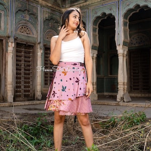 May include: A layered pink skirt with a floral and leaf pattern, paired with a white tank top. The skirt features a wrap design and is adorned with colorful accents. The image also shows the text "Hems Sari Boutique".