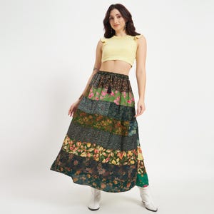 Könnte beinhalten: Langer Patchwork-Rock mit floralen und gemusterten Stoffbahnen in Grün-, Braun- und Gelbtönen. Der Rock hat einen Kordelzug in der Taille und wird mit einem gelben Crop-Top getragen. Der Rock ist im Bohemian-Stil gehalten.