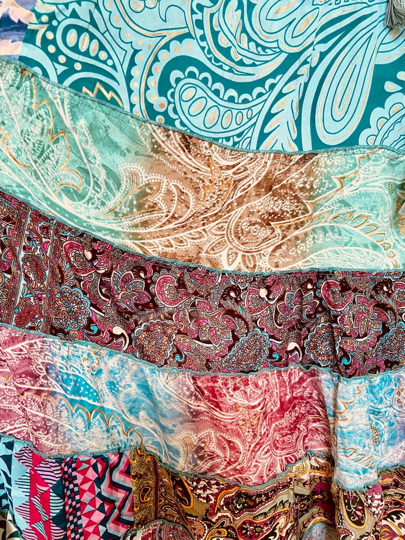 Puede incluir: Primer plano de un textil patchwork con una variedad de estampados de cachemira y geom&eacute;tricos. La tela presenta tonos de verde azulado, marr&oacute;n, rosa y rojo, con una mezcla de texturas y dise&ntilde;os. El textil parece ser una falda o una prenda similar.