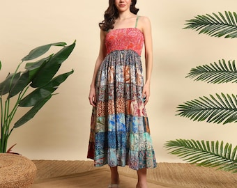May include: A patchwork midi dress with a red, textured bodice and patterned skirt. The skirt features squares of various colors and designs, including blue, brown, and teal. The dress has thin straps and a flowing silhouette, suitable for warm weather.