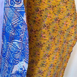May include: Close-up of two fabric panels. One panel is blue with white floral and geometric patterns. The other panel is yellow with a repeating pattern of small, dark shapes and flecks of blue and pink.