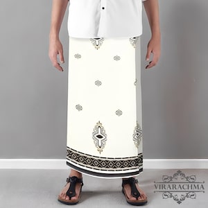 May include: A white sarong with a black and gold geometric pattern at the bottom and decorative motifs. The sarong is worn with a white shirt and black sandals. The brand name "VIRARACHMA" is visible in the bottom right corner.