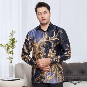 Pode incluir: Uma camisa de manga comprida com fundo preto e roxo com um design de fênix dourado. A camisa tem colarinho e fecho de botões. O texto "VIRARACHMA" é visível no canto inferior direito da imagem.