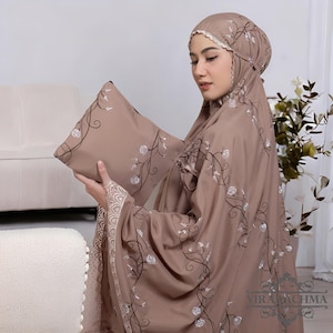 May include: A taupe prayer garment set with floral embroidery. The set includes a head covering and a matching carrying case. The embroidery features white flowers and dark brown stems. The garment has a lace trim.