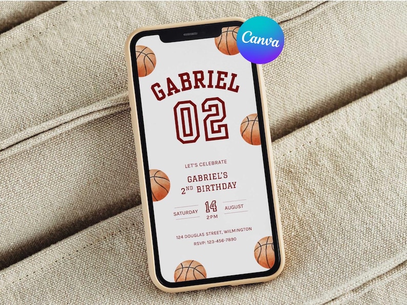 May include: A smartphone displays a basketball-themed birthday invitation. The invitation features the name "GABRIEL" and the number "02" in maroon, along with basketball illustrations. The text reads "LET'S CELEBRATE GABRIEL'S 2ND BIRTHDAY" with date and time details.