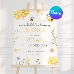 Könnte beinhalten: Ein weißes Schild auf einer Holzstaffelei mit dem Text "our little honey IS ONE!" und "FIRST BEE-DAY!" in goldener Schrift. Das Schild ist mit Aquarellbienen, Waben und Blumen verziert. Das Canva-Logo befindet sich oben rechts.