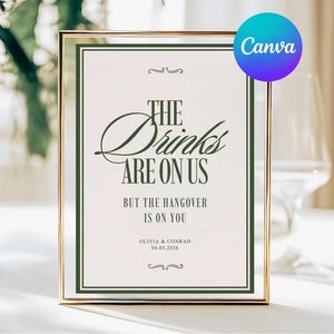 May include: A framed sign with the text "THE Drinks ARE ON US BUT THE HANGOVER IS ON YOU". The sign has a gold frame and a green border. The text is in a decorative font. The sign also includes the names Olivia & Conrad and the date 04.05.2026.