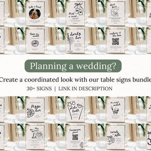 May include: A collection of wedding table signs with various illustrations and text, including "Planning a wedding?" and "Create a coordinated look with our table signs bundle!" The signs are in gold frames.