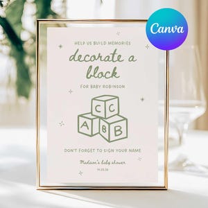 May include: A framed sign with gold trim, featuring the text "decorate a block" for a baby shower. The sign includes a graphic of stacked alphabet blocks and the text "Don't forget to sign your name."