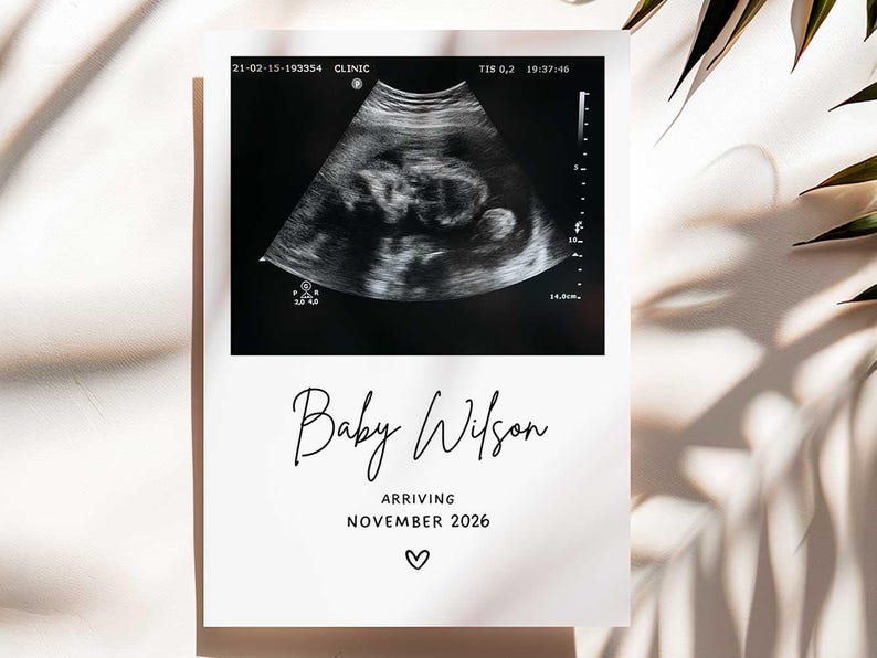 May include: A black and white sonogram image on a white card. The card reads "Baby Wilson Arriving November 2026" in elegant script, with a small heart symbol below the text. The image is a pregnancy announcement.