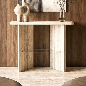 Puede incluir: Un pasillo interior con paneles de madera y una paleta de colores neutros. Una consola de piedra alberga jarrones decorativos y un jarrón de cristal con ramas. Una gran pintura abstracta cuelga de la pared, añadiendo un punto focal.