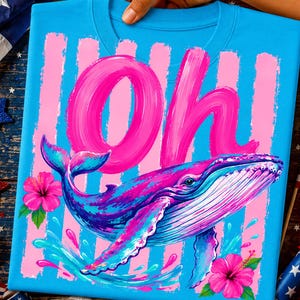 Pu&ograve; includere: Una t-shirt blu brillante con una grande scritta rosa a pennellate che recita "Oh" sopra un'illustrazione colorata di una balena. Il design include strisce verticali rosa, due vivaci fiori di ibisco rosa e spruzzi d'acqua blu.