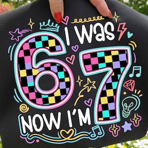 May include: Black fabric with the text "I WAS 67 NOW I'M" in white, with colorful accents. The numbers 6 and 7 are checkered with pink, yellow, black, and teal squares. The design includes stars, hearts, and musical notes.
